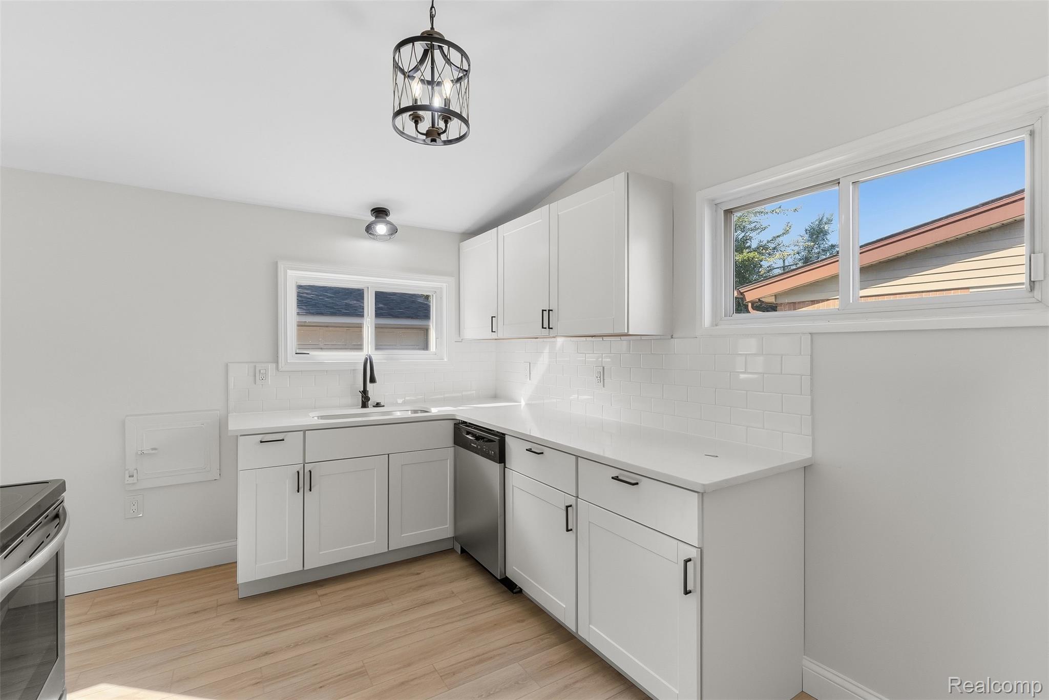 9101 Merriman Road Livonia, MI 48150 - Photo 25 of 41 White shaker cabinetry, light-toned wood-finish flooring, white subway tile backsplash, white countertops, and stainless steel dishwasher