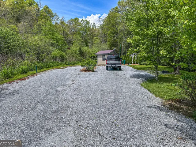a view of a house with truck parked on a road near a forest