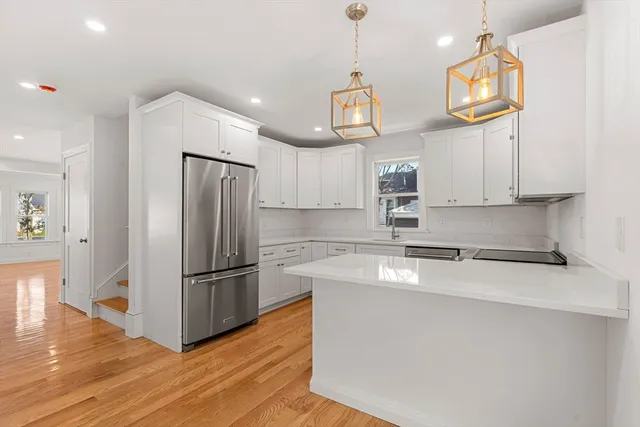 a kitchen with stainless steel appliances granite countertop a refrigerator a sink dishwasher a microwave oven a stove and white cabinets with wooden floor