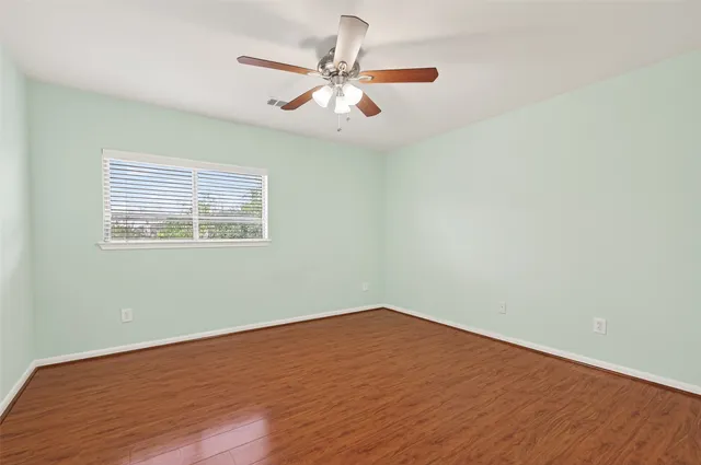 an empty room with wooden floor fan and windows