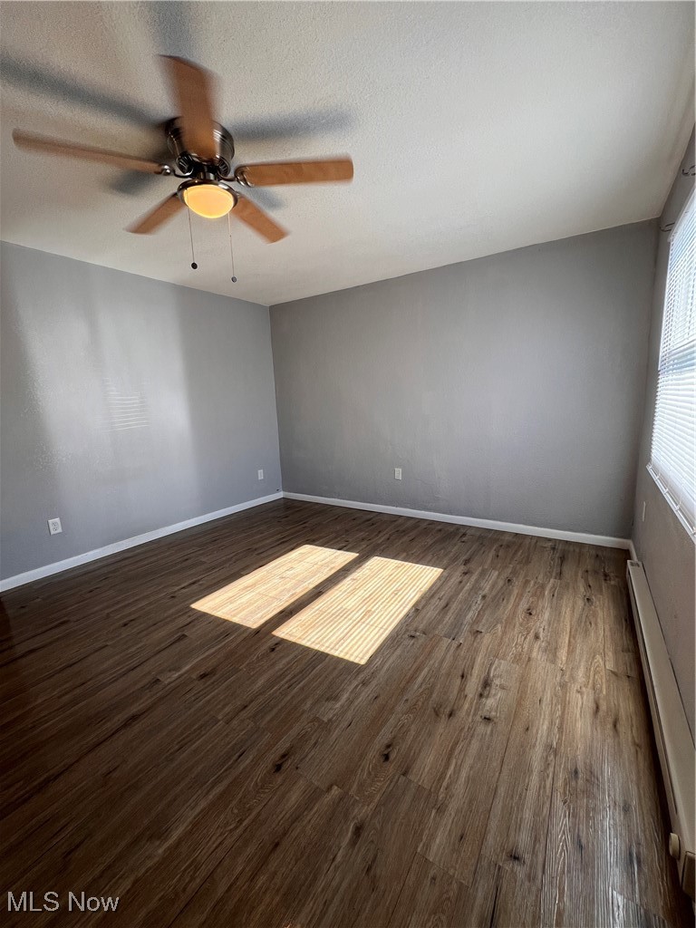 1724 Youngstown Kingsville Road, Unit 4 Vienna, OH 44473 - Photo 4 of 11 Spare room featuring baseboards, a ceiling fan, a baseboard heating unit, and dark wood-style floors