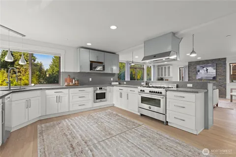 a kitchen with stainless steel appliances granite countertop a stove top oven a sink dishwasher and white cabinets with wooden floor