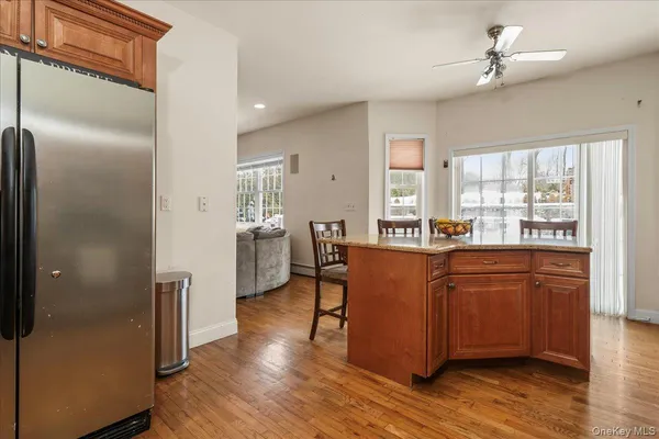 a living room with stainless steel appliances granite countertop a refrigerator a sink dishwasher a stove and a dining table with wooden floor