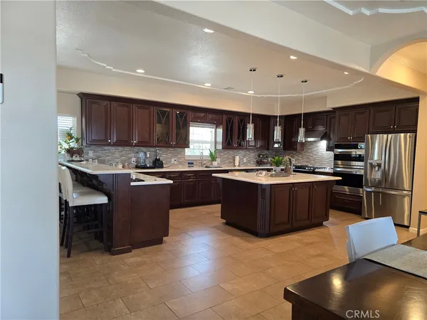 a kitchen with stainless steel appliances granite countertop a stove a sink a refrigerator a microwave oven and a dining table with wooden cabinet