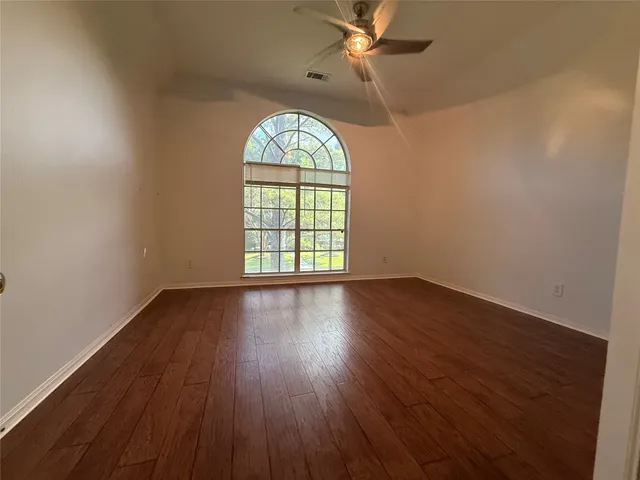 an empty room with wooden floor fan and windows
