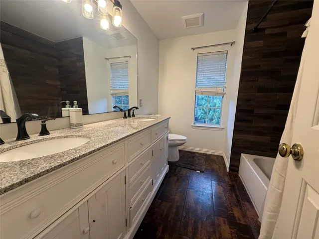 a bathroom with a granite countertop double vanity sink a mirror and a bathtub