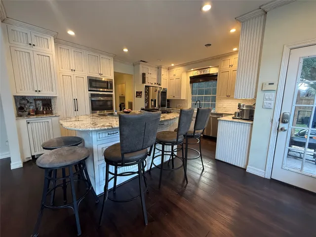 a kitchen with stainless steel appliances kitchen island granite countertop a dining table chairs refrigerator sink and cabinets