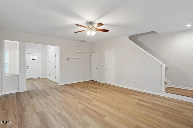 a view of an empty room with wooden floor and a ceiling fan