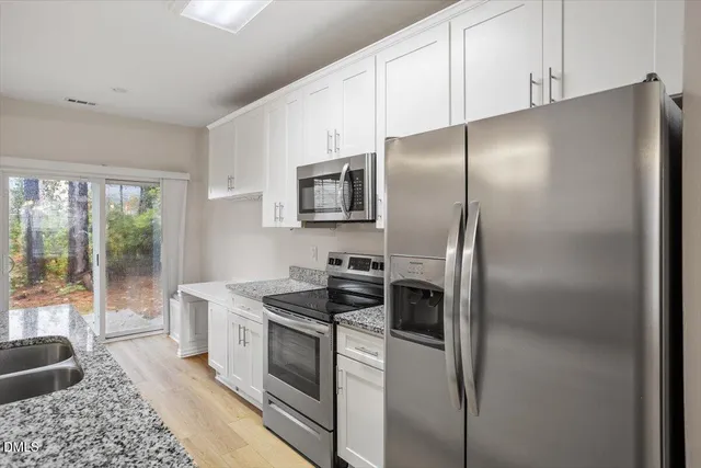 a kitchen with stainless steel appliances granite countertop a refrigerator a stove a sink and white cabinets with wooden floor