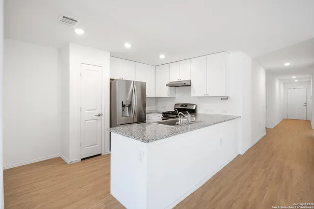 a kitchen with stainless steel appliances granite countertop a refrigerator a sink a stove a microwave and white cabinets with wooden floor