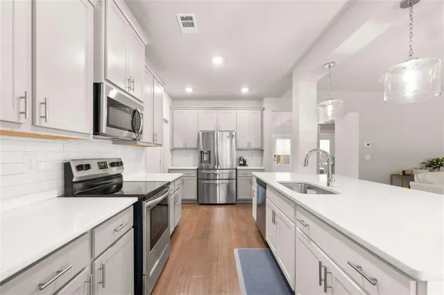 a kitchen with stainless steel appliances a sink dishwasher a stove top oven a refrigerator with white cabinets and wooden floor