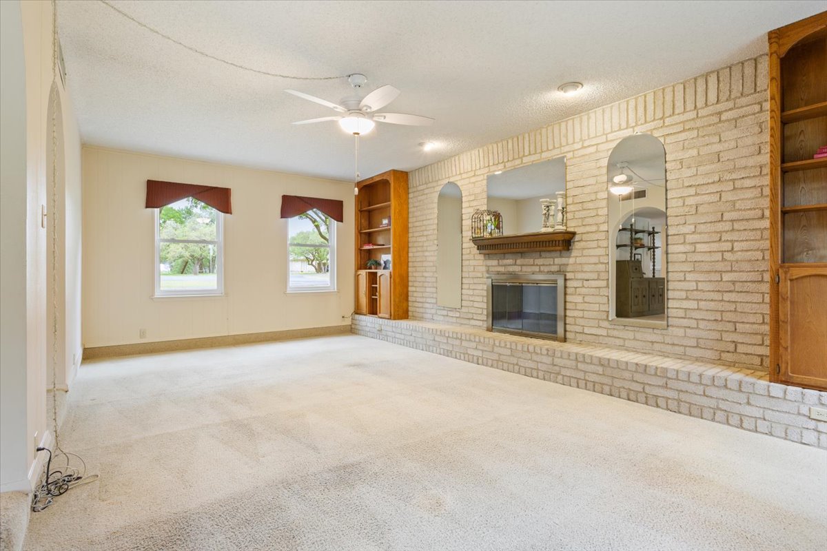 4015 Ramada Trail Georgetown, TX 78628 - Photo 11 of 35 Unfurnished living room featuring built in features, ceiling fan, carpet flooring, a fireplace, and a textured ceiling