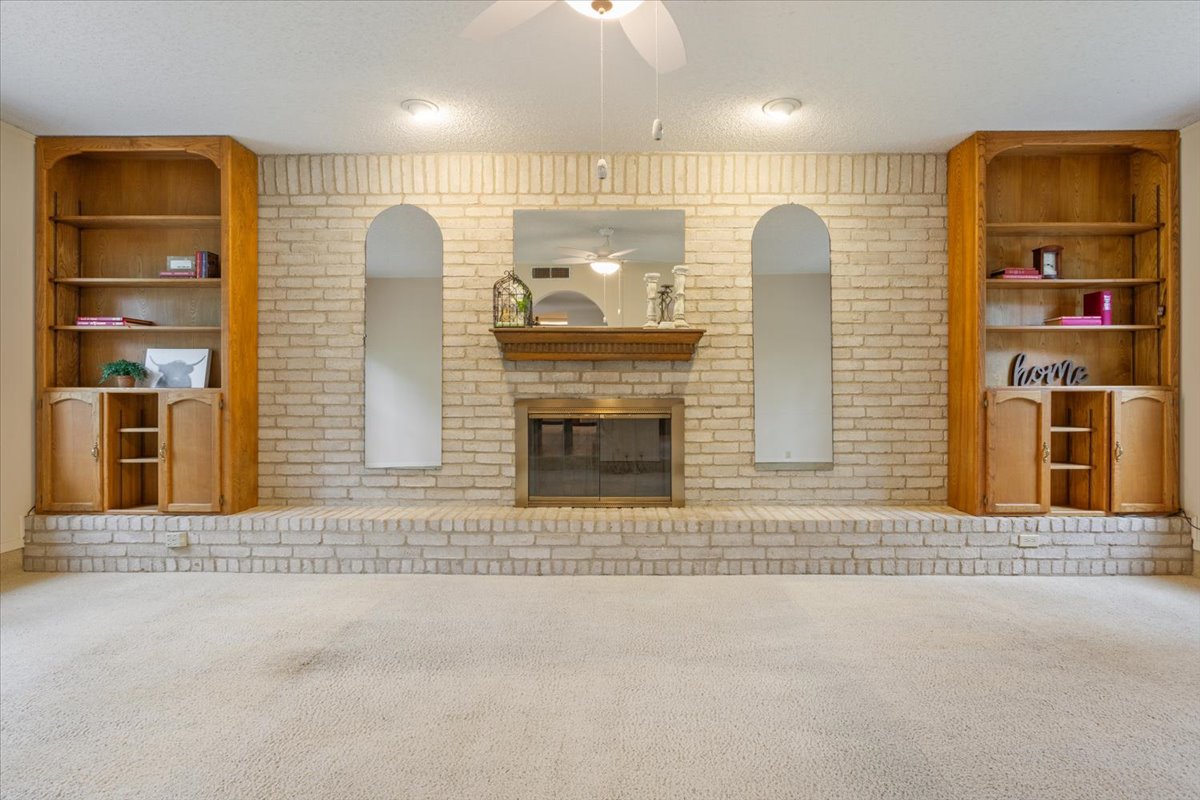 4015 Ramada Trail Georgetown, TX 78628 - Photo 12 of 35 Unfurnished living room with built in features, carpet flooring, a brick fireplace, ceiling fan, and a textured ceiling