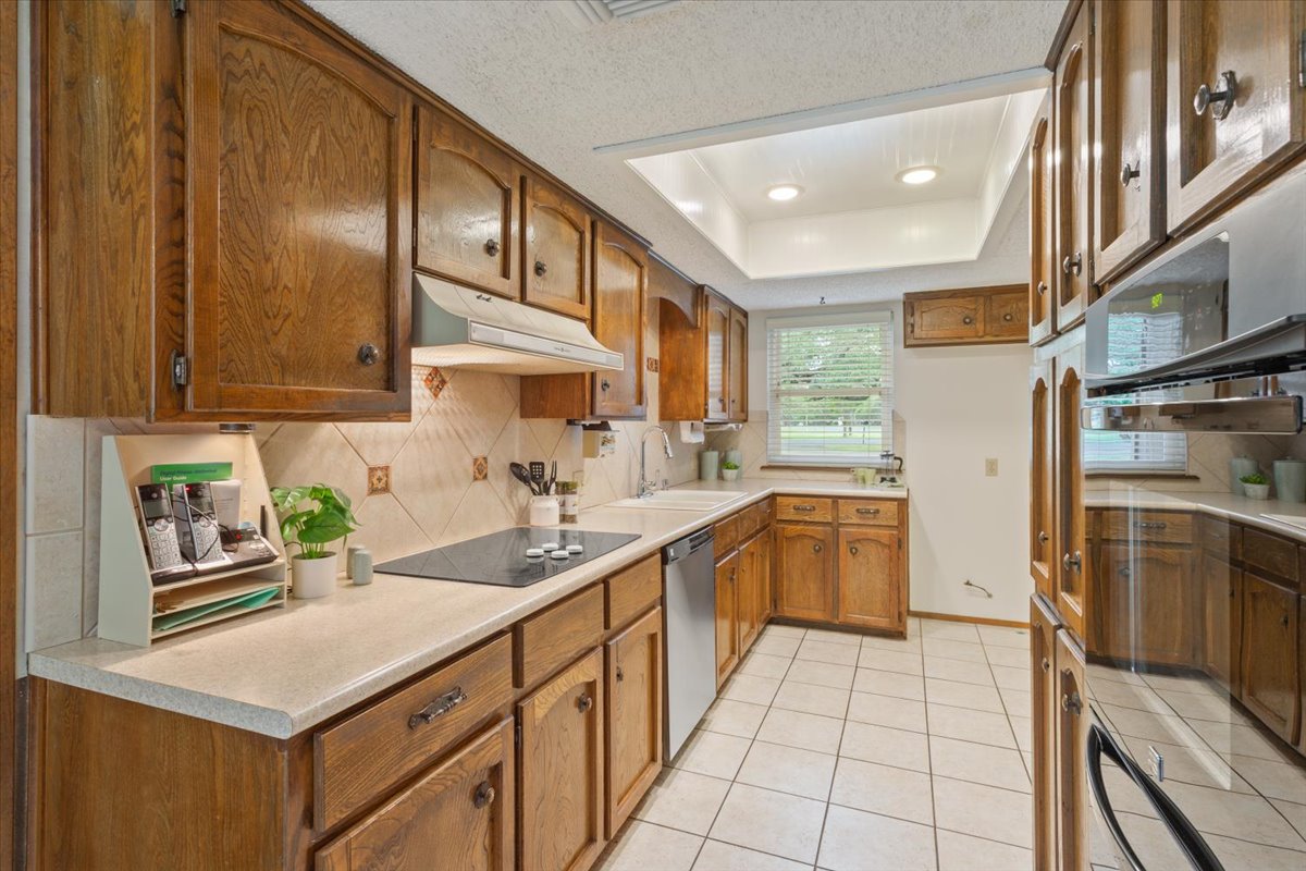 4015 Ramada Trail Georgetown, TX 78628 - Photo 14 of 35 Kitchen with wood finish cabinets, light countertops, a raised ceiling, light tile patterned floors, and black electric cooktop