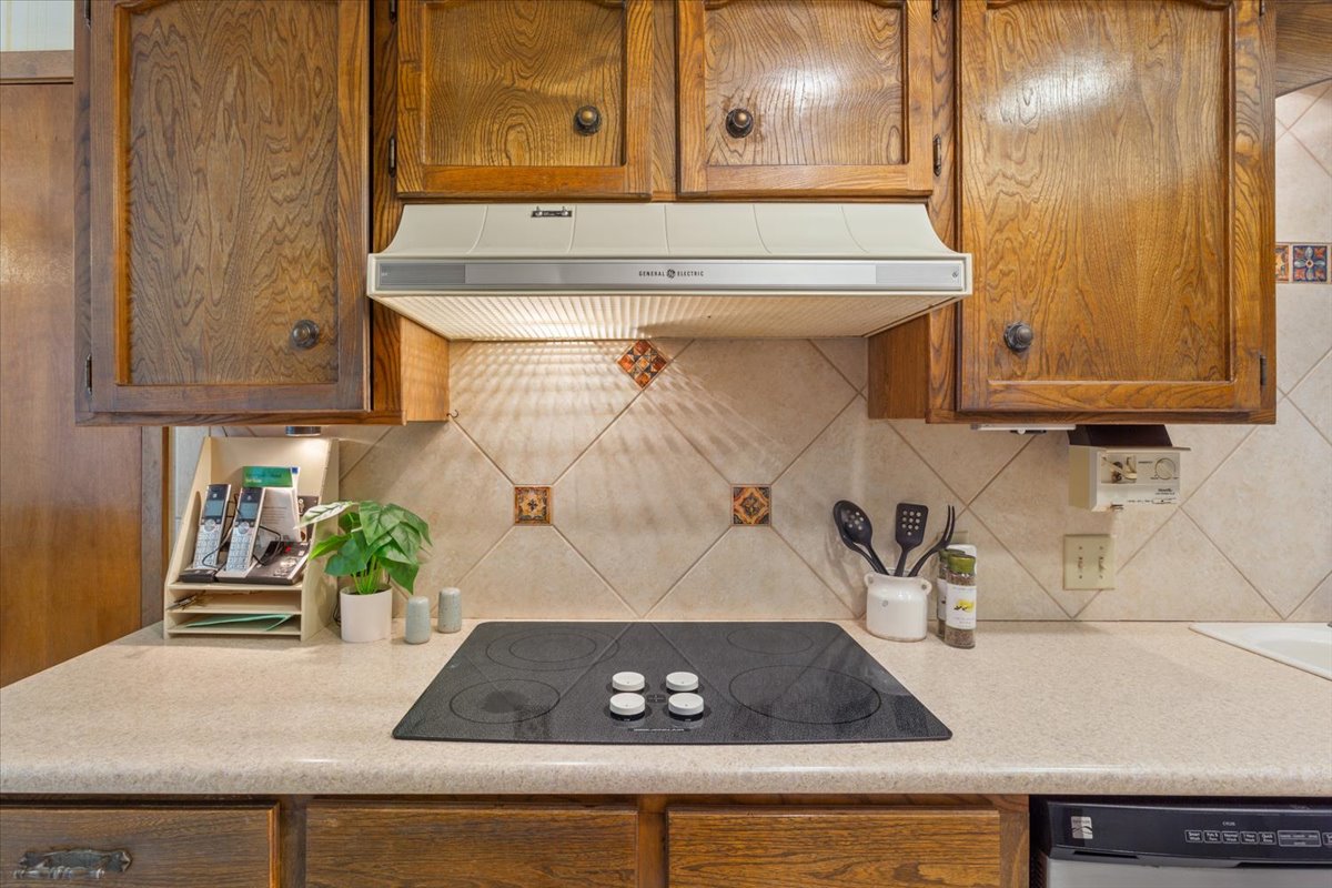 4015 Ramada Trail Georgetown, TX 78628 - Photo 15 of 35 Kitchen with wood finish cabinets, light countertops, black electric cooktop, ventilation hood, and dishwashing machine