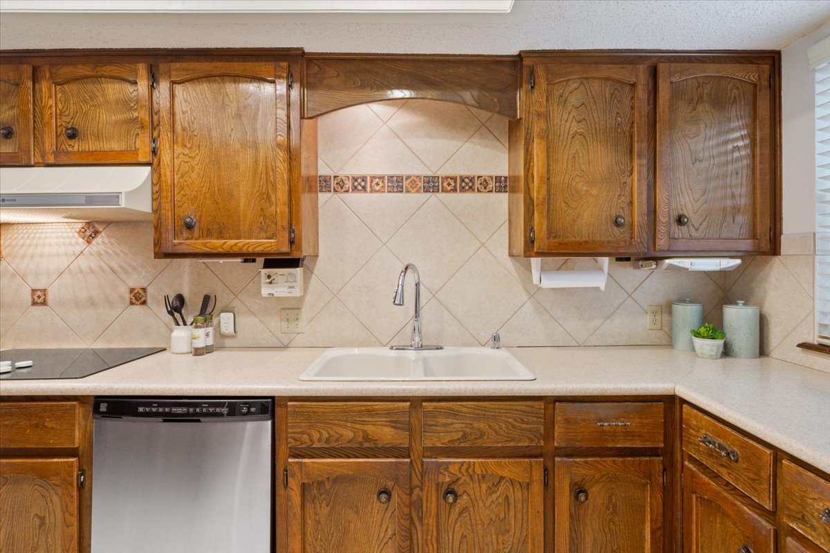 4015 Ramada Trail Georgetown, TX 78628 - Photo 16 of 35 Kitchen featuring wood finish cabinetry, stainless steel dishwasher, light countertops, range hood, and tasteful backsplash