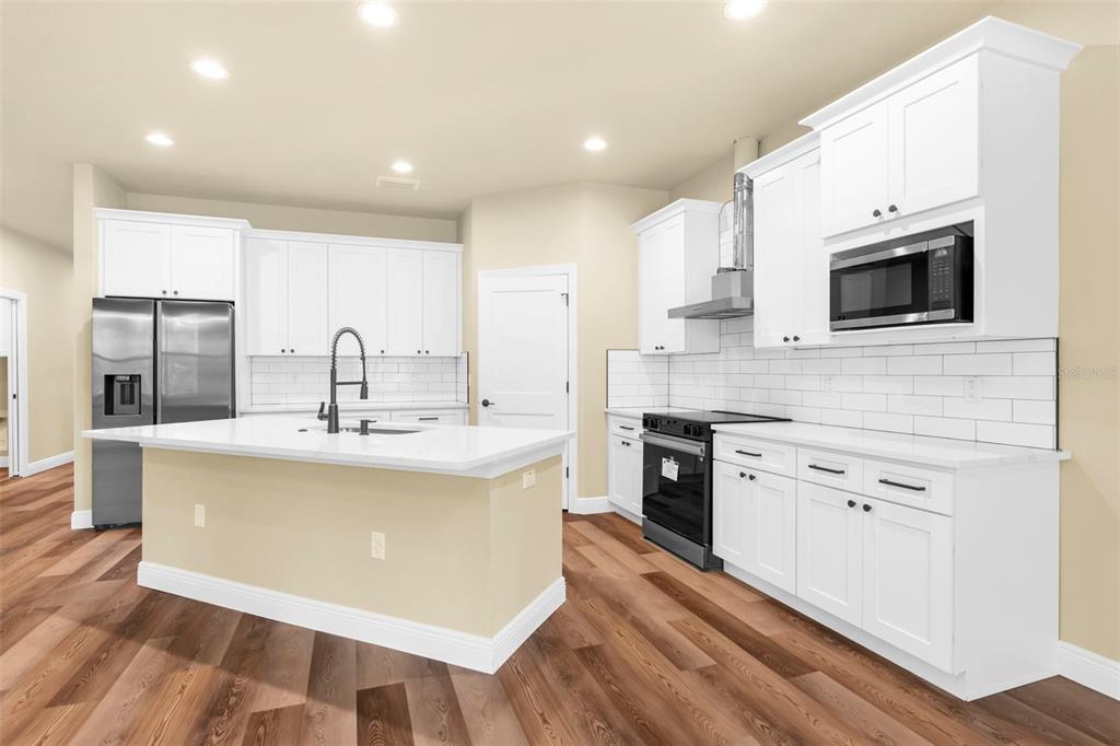 16143 Penn State Road Weeki Wachee, FL 34614 - Photo 12 of 45 a kitchen with stainless steel appliances white cabinets a sink dishwasher a stove and a refrigerator with wooden floor