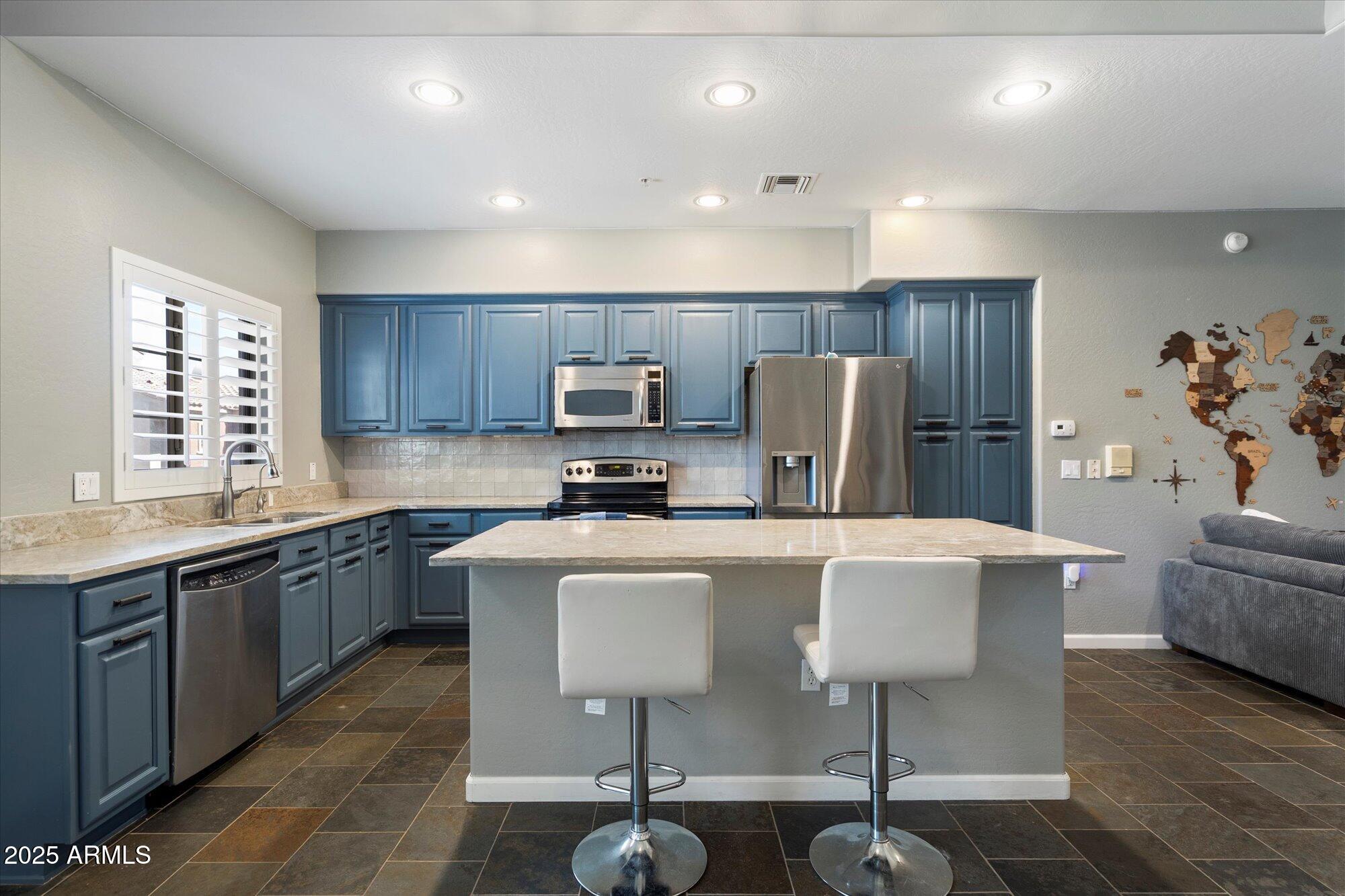 3935 East Rough Rider Road, Unit 1164 Phoenix, AZ 85050 - Photo 7 of 20 a kitchen with kitchen island a white counter top space cabinets and stainless steel appliances