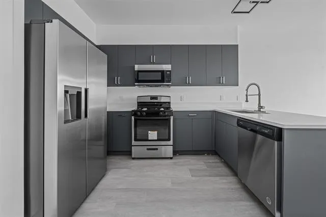 a kitchen with stainless steel appliances a sink a stove a microwave a refrigerator a counter top space and cabinets