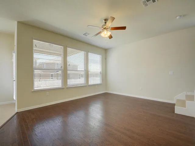 an empty room with wooden floor fan and windows