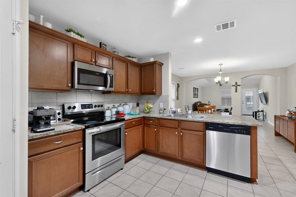 1409 Slate Street Princeton, TX 75407 - Photo 11 of 36 Kitchen featuring wood cabinetry, stainless steel appliances, granite-finish countertops, and tile flooring