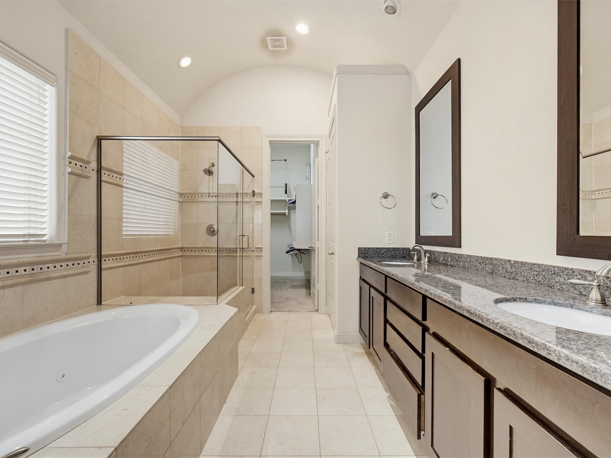 9427 London Bridge Station Houston, TX 77045 - Photo 23 of 30 This is a spacious and modern bathroom featuring a large soaking tub, a separate glass-enclosed shower, dual sinks with granite countertops, and ample cabinet space. The neutral tile and natural light create an inviting atmosphere.