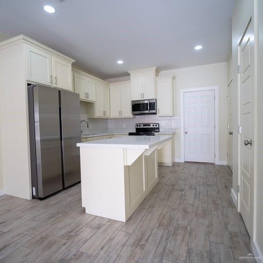 3052 Briggs Road, Unit C Weslaco, TX 78596 - Photo 5 of 16 Bright kitchen featuring an island with a light-toned countertop, ample cream-colored cabinetry, stainless steel appliances, a white subway tile backsplash, and wood-finish flooring
