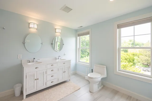 a bathroom with a toilet a sink a mirror a window and a window