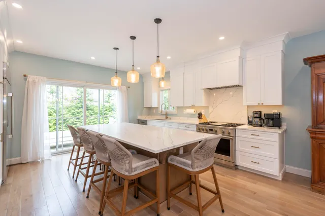 a kitchen with stainless steel appliances granite countertop a stove a refrigerator a kitchen island a table and chairs with wooden floor