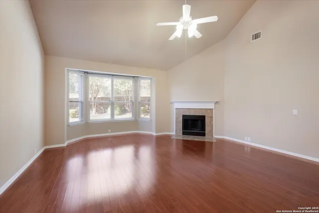 an empty room with wooden floor fireplace and windows