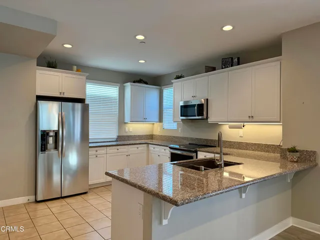 a kitchen with stainless steel appliances granite countertop a refrigerator a stove a sink a microwave and white cabinets