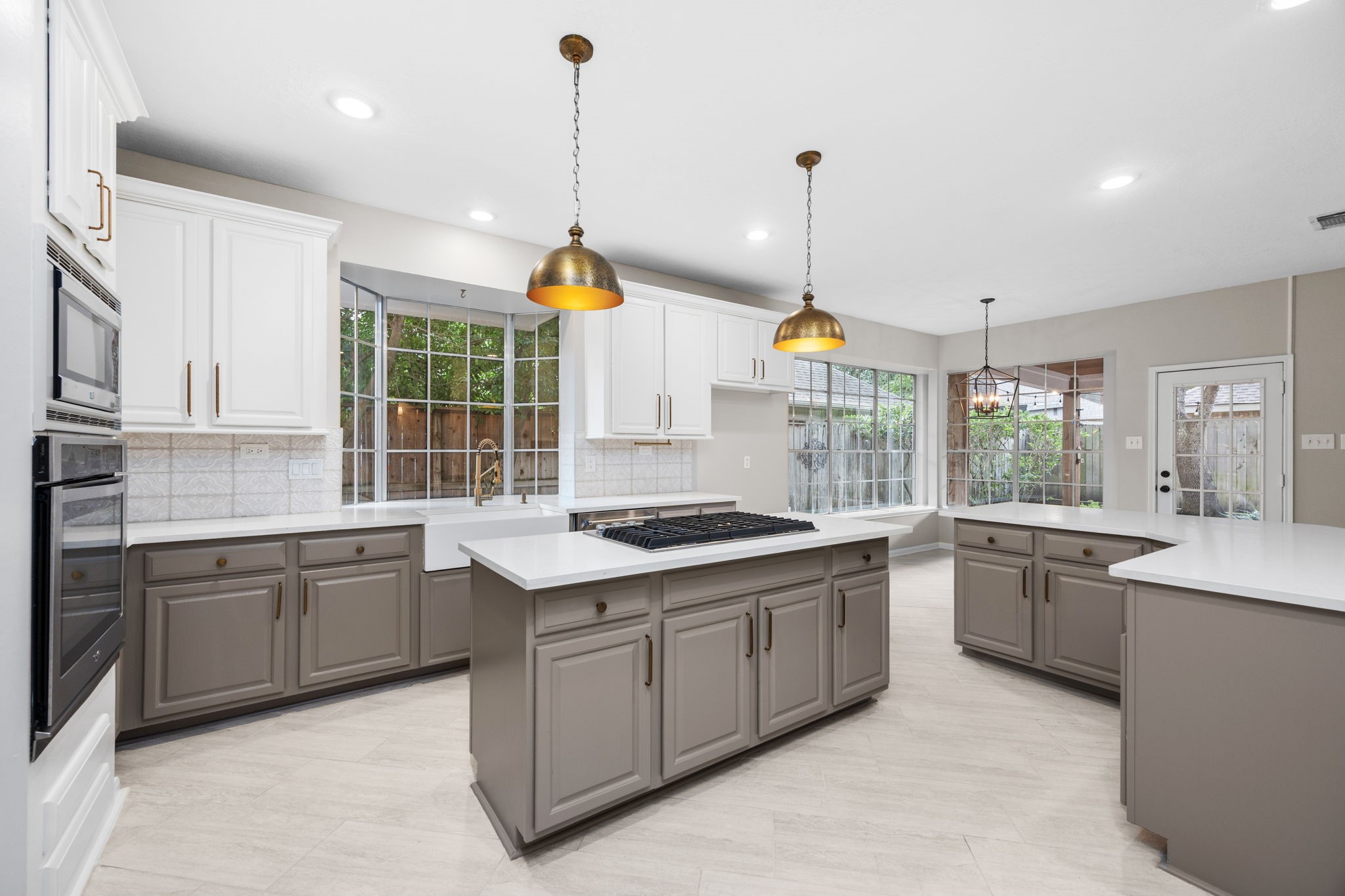 9015 Rhapsody Lane Houston, TX 77040 - Photo 12 of 39 This beautifully updated kitchen features crisp white cabinetry paired with warm neutral lower cabinets, sleek quartz countertops, and stylish brass accents. A large center island with gas cooktop provides plenty of prep space, while expansive windows fill the kitchen and adjoining breakfast area with natural light and views of the backyard.