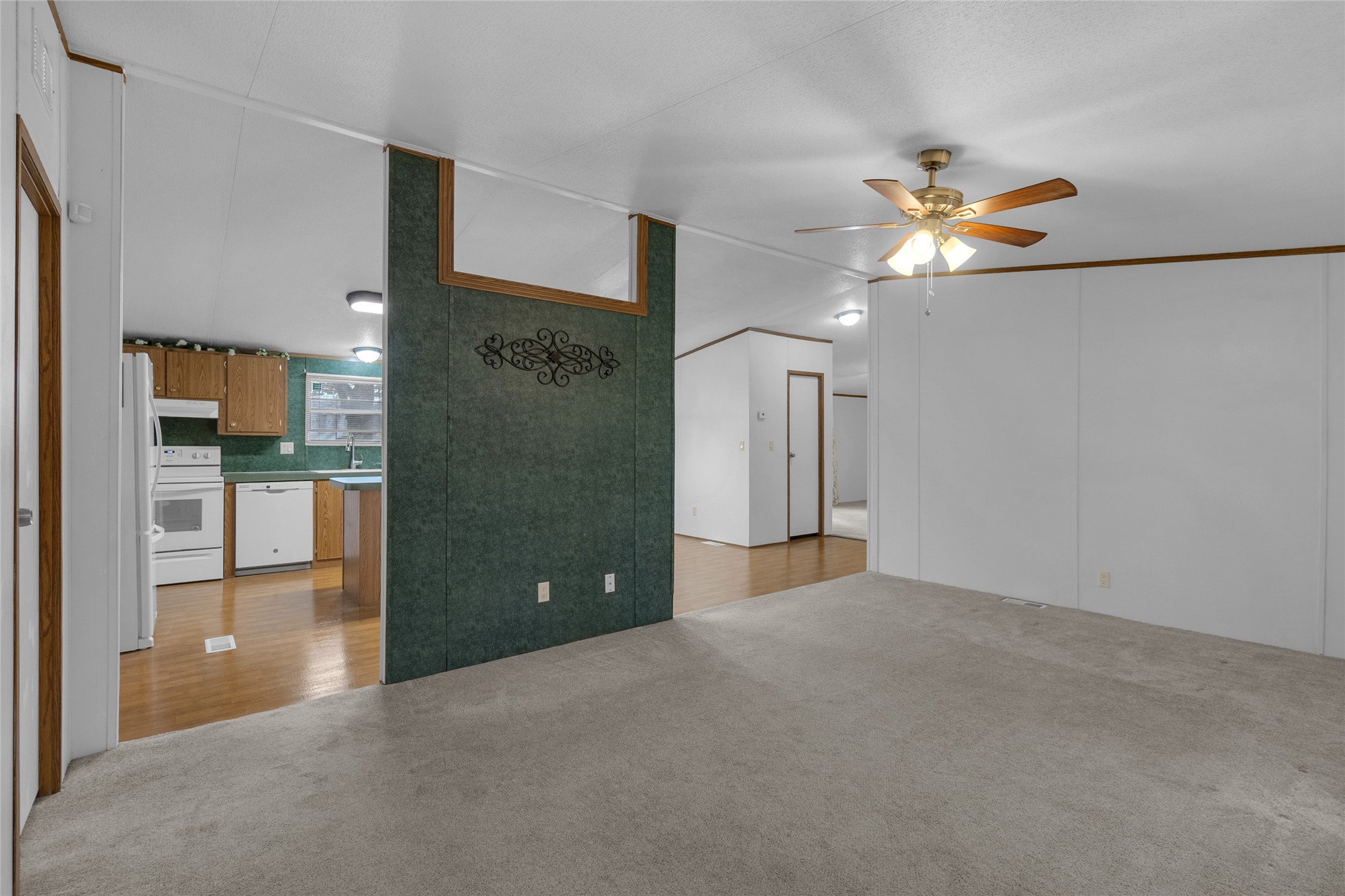 22094 Spear Road Porter, TX 77365 - Photo 16 of 45 This photo features an open living space with a ceiling fan, neutral carpet, and an adjacent kitchen with wood flooring and appliances. The area has clean, white walls and a decorative green accent wall, creating a warm and inviting atmosphere.
