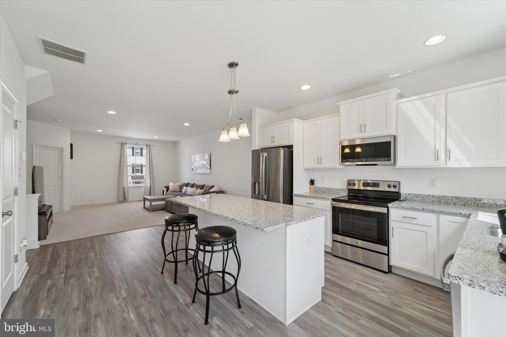 65 Aviary Road Thorofare, NJ 08086 - Photo 7 of 16 a kitchen with stainless steel appliances kitchen island granite countertop a refrigerator a stove a sink a dining table and chairs with wooden floor