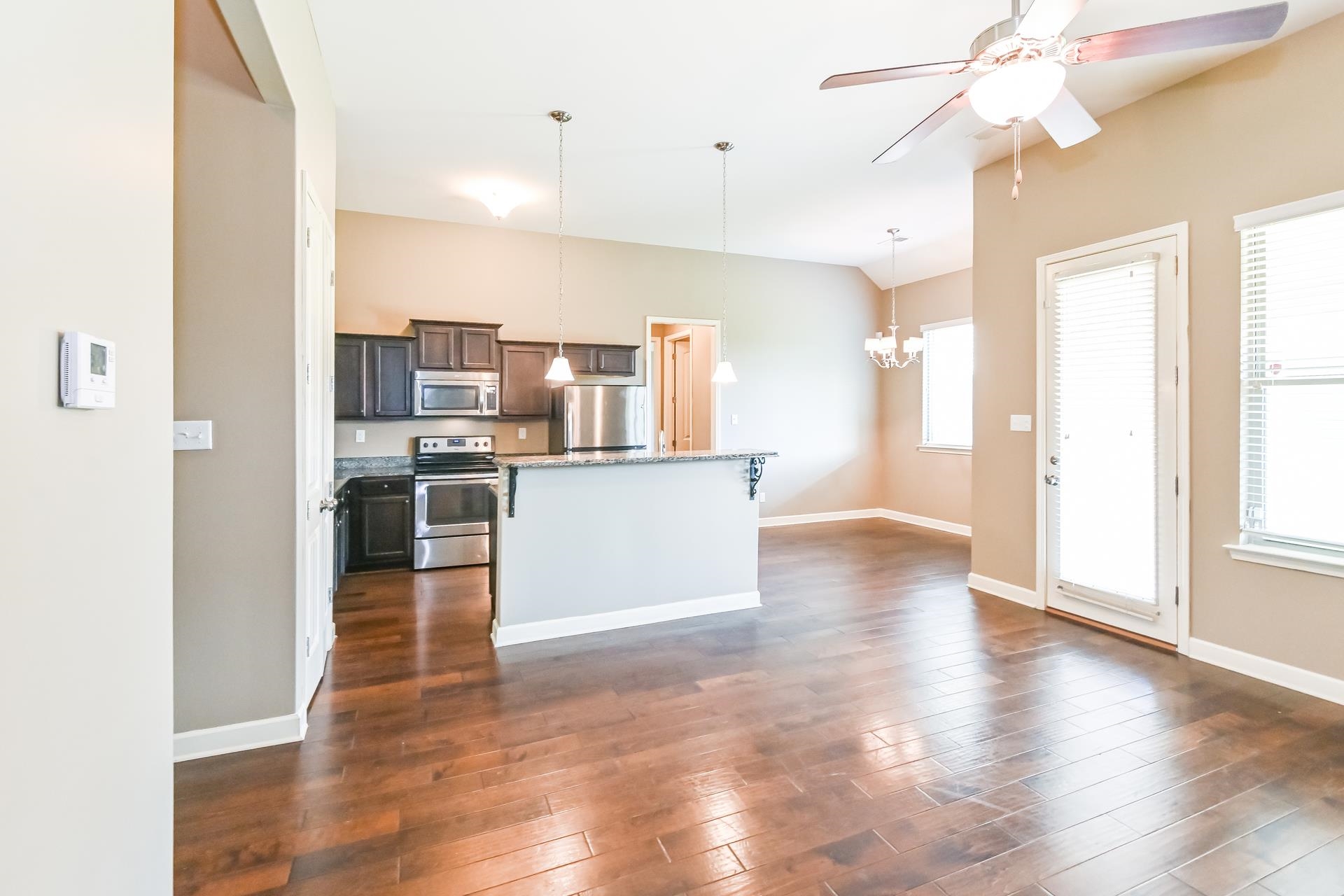 Kitchen with ceiling fan with notable chandelier, hanging light fixtures, a center island, dark wood-type flooring, and appliances with stainless steel finishes