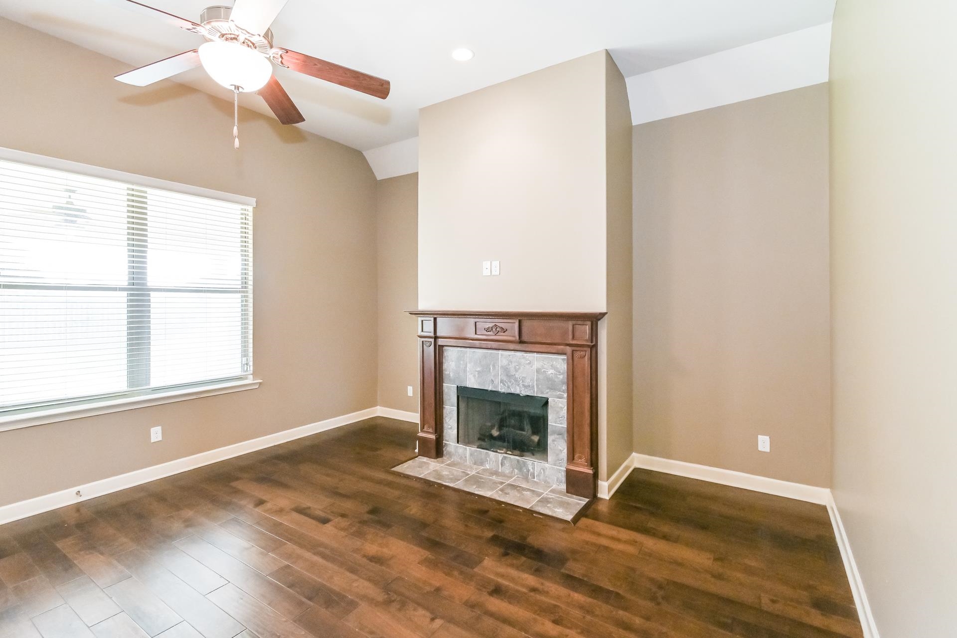 Unfurnished living room featuring dark hardwood / wood-style flooring, a tiled fireplace, and ceiling fan