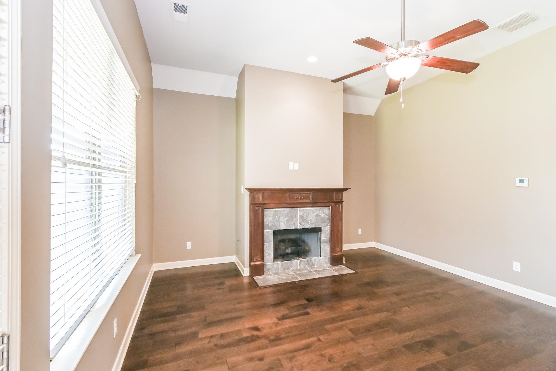 Unfurnished living room featuring dark hardwood / wood-style floors, ceiling fan, and a tiled fireplace