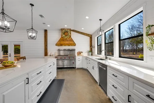 a large white kitchen with stainless steel appliances granite countertop a stove a sink and a window
