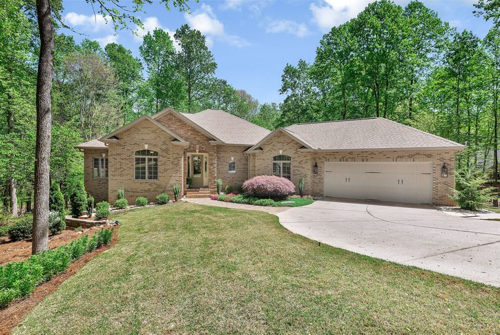 This charming brick home is nestled among lush trees, featuring a well-maintained lawn and an inviting entrance.