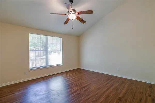 an empty room with wooden floor ceiling fan and windows
