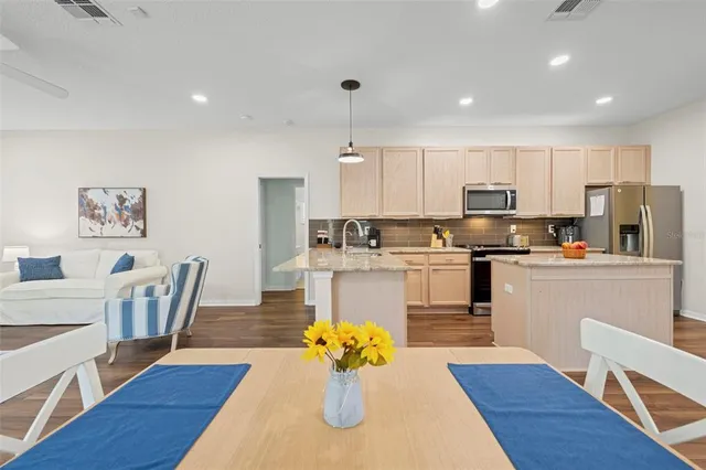 a kitchen with stainless steel appliances granite countertop a refrigerator a stove top oven and a dining table with wooden floor