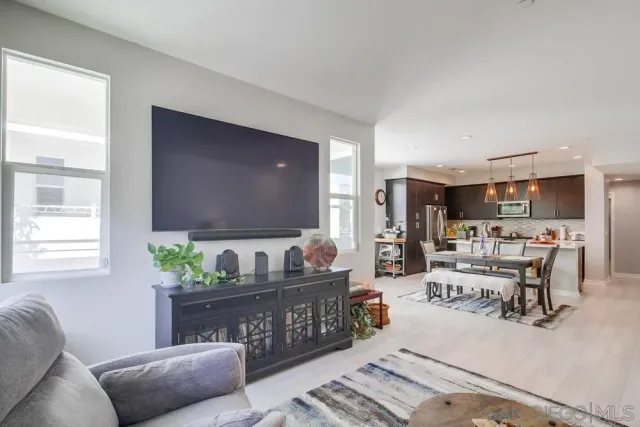 a living room with stainless steel appliances kitchen island granite countertop a refrigerator a stove a sink and a dining table with wooden floor