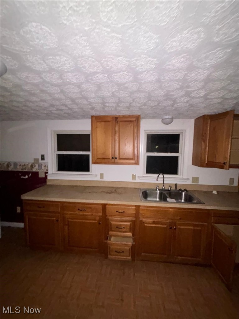 Kitchen featuring a textured ceiling, wood finished floors, a sink, and brown cabinets