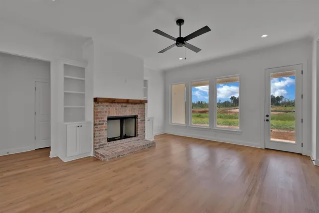 a view of a livingroom with a fireplace a ceiling fan and windows