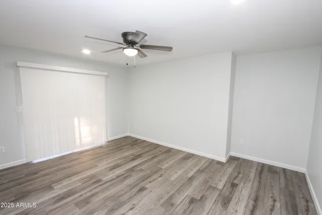 an empty room with wooden floor fan and windows