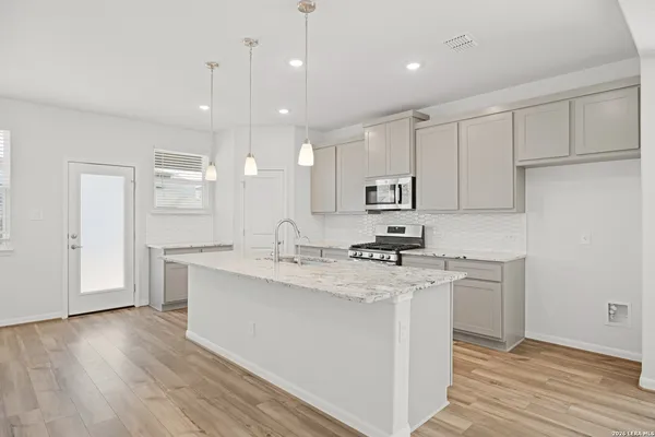a kitchen with stainless steel appliances granite countertop a sink a stove a refrigerator and white cabinets with wooden floor