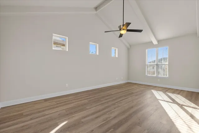 an empty room with wooden floor ceiling fan and windows