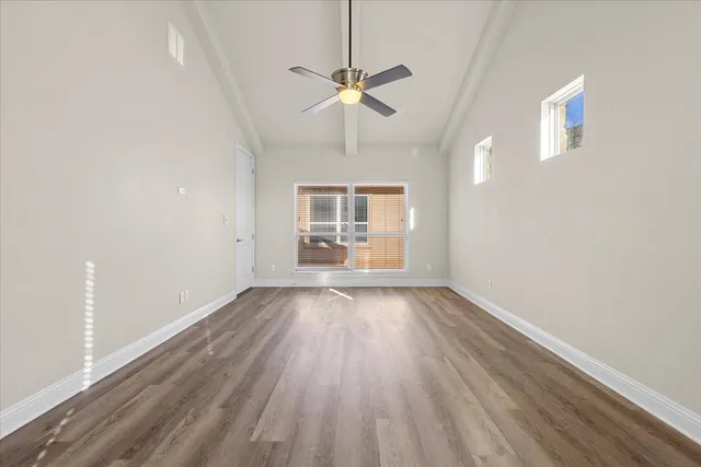an empty room with wooden floor chandelier fan and windows
