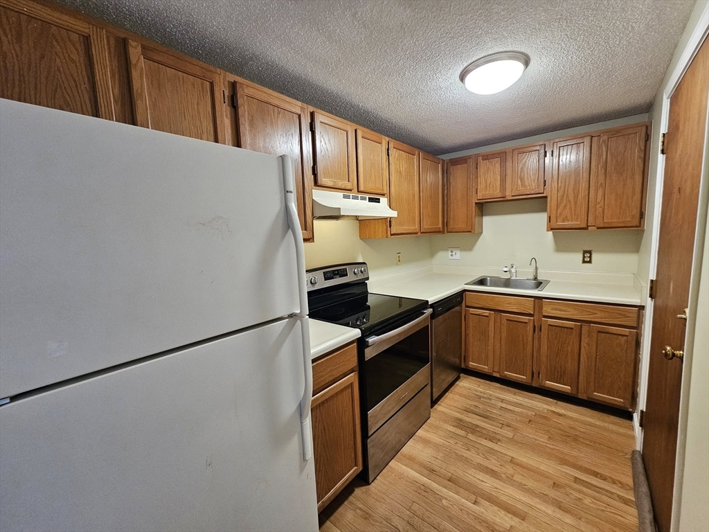 35 Prospect Street, Unit 215 Woburn, MA 01801 - Photo 7 of 37 a kitchen with stainless steel appliances granite countertop a refrigerator a sink dishwasher a stove with wooden cabinets and floors
