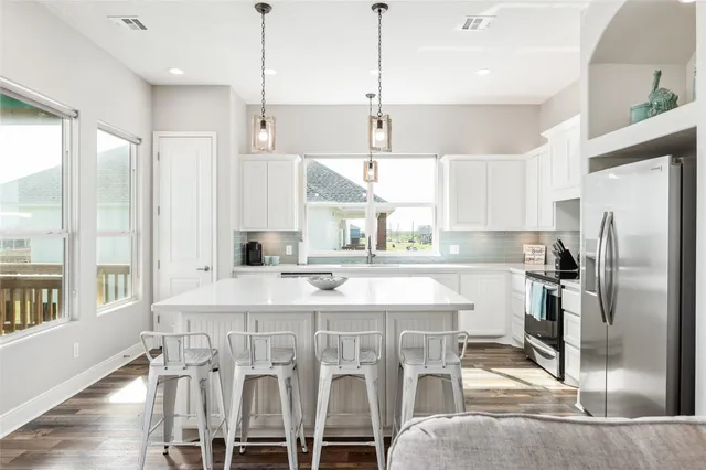 a kitchen with stainless steel appliances kitchen island granite countertop a refrigerator a stove and white cabinets with wooden floor